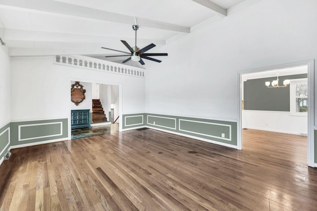 unfurnished living room featuring beamed ceiling, ceiling fan with notable chandelier, wood finished floors, and stairway