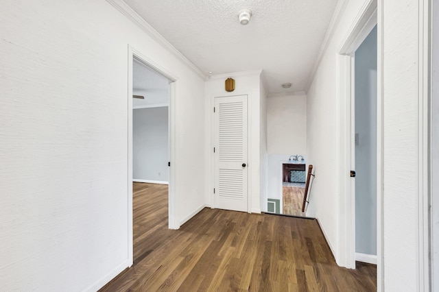 hall featuring baseboards, a textured ceiling, ornamental molding, and dark wood-style flooring