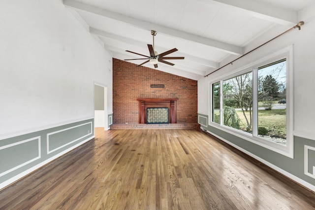 unfurnished living room with wood finished floors, wainscoting, a fireplace, ceiling fan, and vaulted ceiling with beams