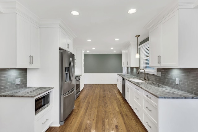 kitchen with appliances with stainless steel finishes, wood finished floors, stone countertops, white cabinetry, and a sink