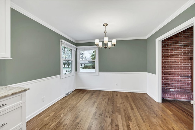 unfurnished dining area featuring an inviting chandelier, crown molding, wood finished floors, and baseboards