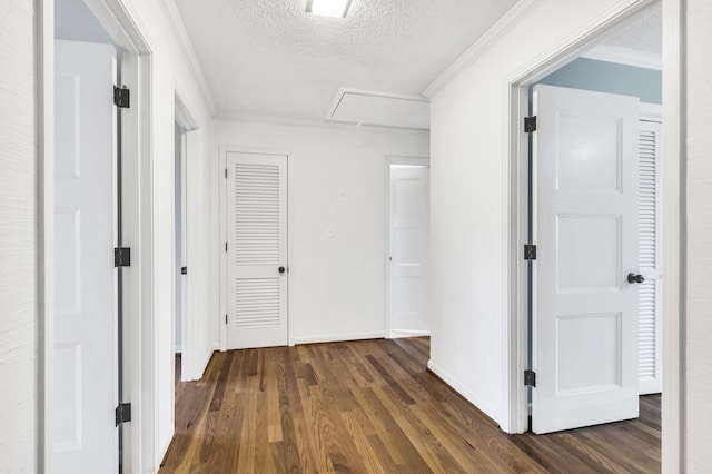 hall with dark wood-type flooring, attic access, crown molding, and a textured ceiling