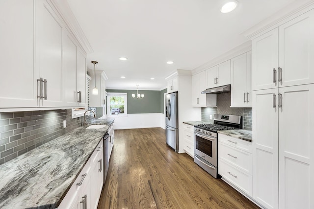 kitchen featuring under cabinet range hood, a sink, white cabinetry, appliances with stainless steel finishes, and crown molding