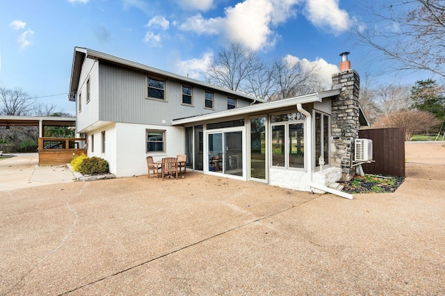 back of property with a deck, a chimney, a patio, and a sunroom