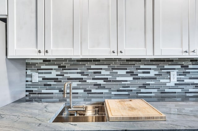 details featuring light stone counters, decorative backsplash, white cabinets, and a sink