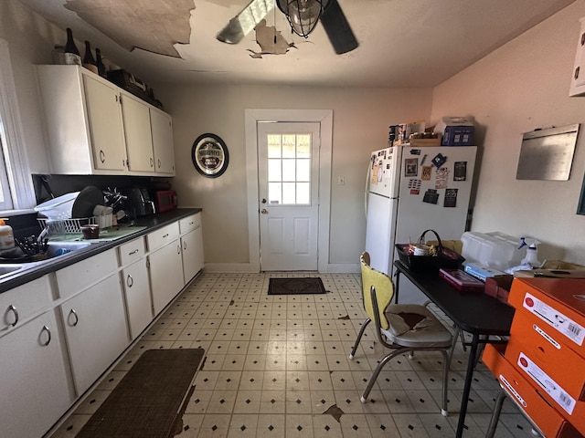 kitchen featuring light floors, freestanding refrigerator, ceiling fan, white cabinets, and dark countertops