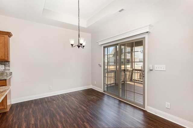 unfurnished dining area with baseboards, visible vents, a tray ceiling, dark wood-type flooring, and a notable chandelier