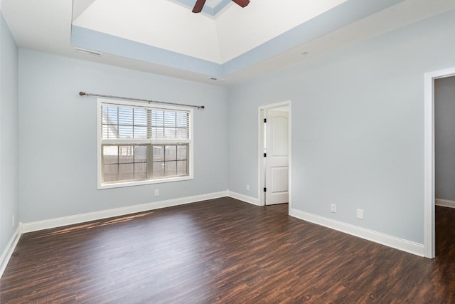 spare room featuring a ceiling fan, dark wood-style floors, visible vents, baseboards, and a raised ceiling