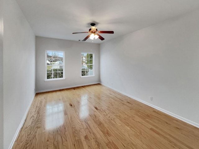 spare room with baseboards, light wood-style floors, and a ceiling fan