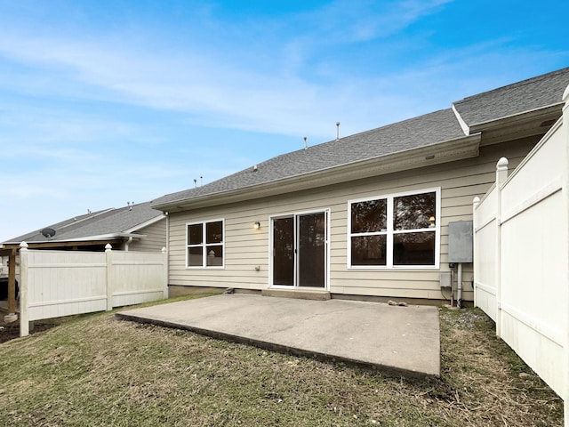 rear view of house featuring fence, roof with shingles, a lawn, and a patio area