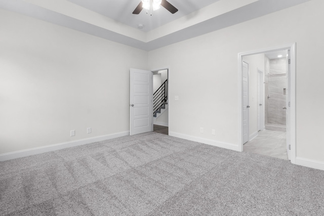 unfurnished bedroom featuring ensuite bath, a tray ceiling, baseboards, and carpet floors