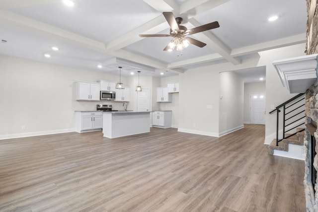 unfurnished living room with baseboards, beam ceiling, stairway, and light wood finished floors