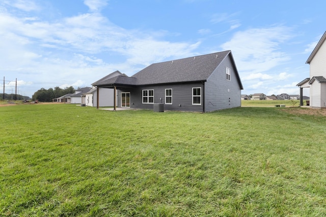 back of property with a lawn, a shingled roof, and central AC