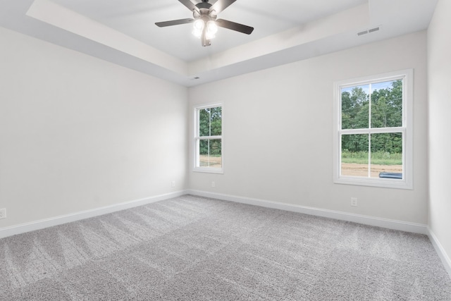 carpeted empty room with a tray ceiling, visible vents, baseboards, and ceiling fan