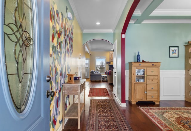 entrance foyer featuring dark wood finished floors, arched walkways, wainscoting, crown molding, and a decorative wall