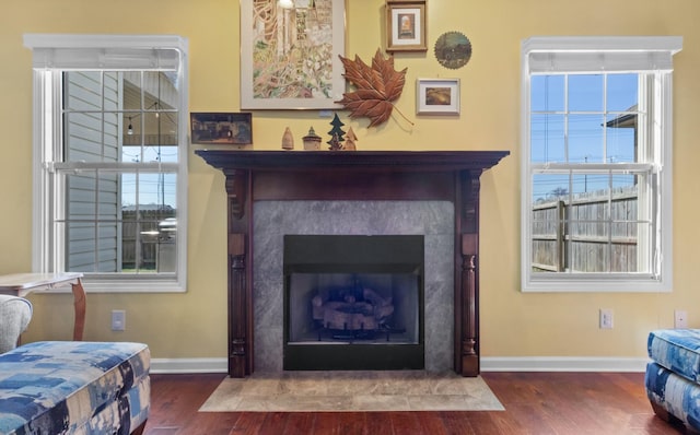 living room featuring a wealth of natural light, a fireplace with flush hearth, baseboards, and wood finished floors