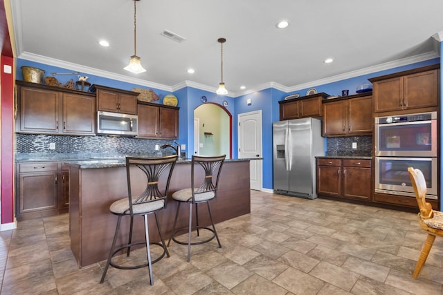 kitchen featuring visible vents, a kitchen bar, hanging light fixtures, appliances with stainless steel finishes, and arched walkways