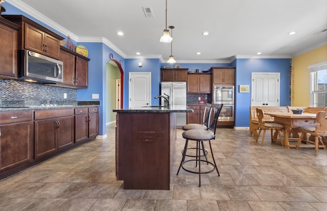 kitchen featuring visible vents, dark stone counters, arched walkways, appliances with stainless steel finishes, and a kitchen bar