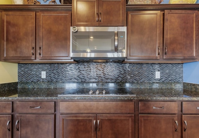 kitchen with cooktop, stainless steel microwave, dark stone countertops, and decorative backsplash