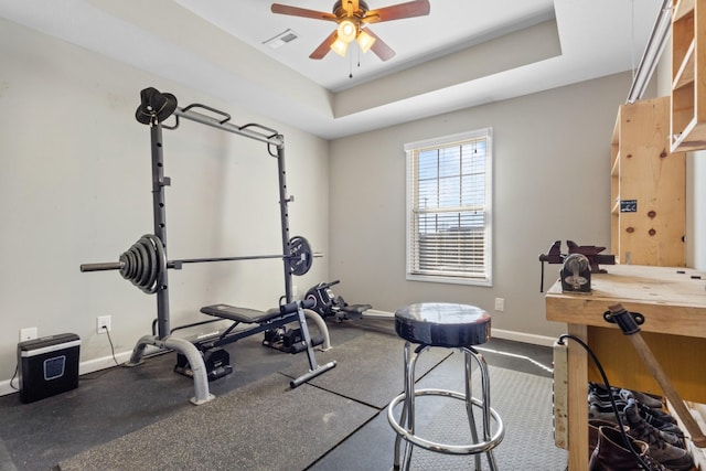 exercise area with a tray ceiling, baseboards, visible vents, and ceiling fan