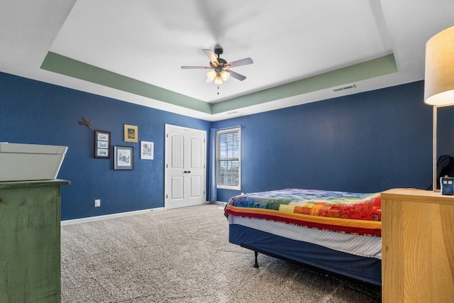 bedroom with visible vents, a tray ceiling, carpet flooring, baseboards, and ceiling fan