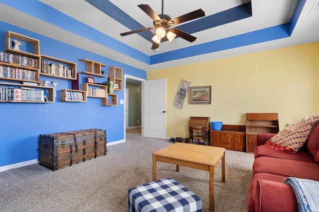 carpeted living area featuring a raised ceiling, baseboards, and ceiling fan