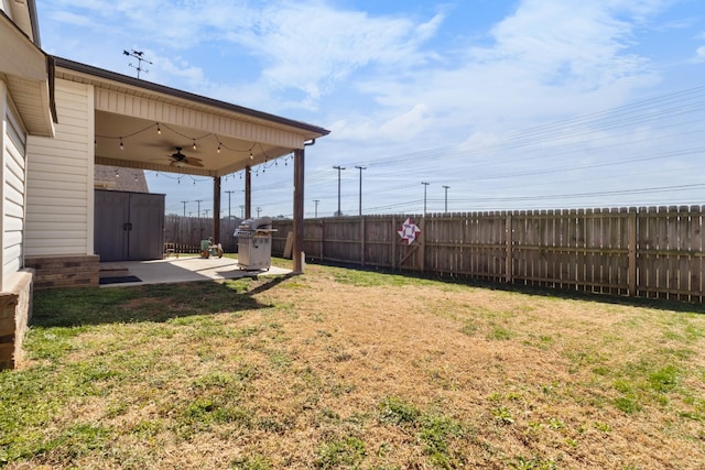 view of yard with an outbuilding, a ceiling fan, a fenced backyard, a storage unit, and a patio area