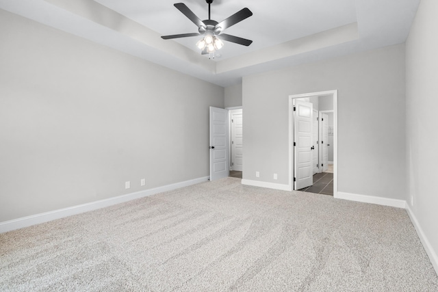 unfurnished bedroom with ceiling fan, baseboards, carpet floors, ensuite bath, and a raised ceiling