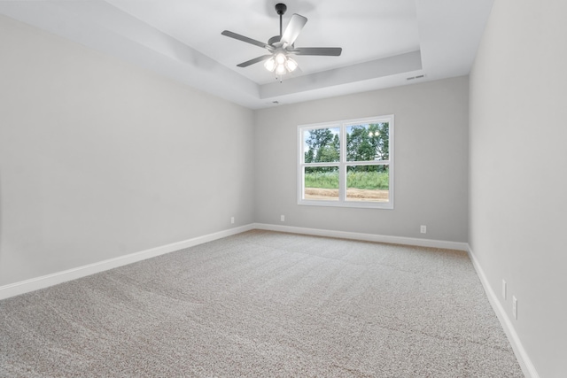 empty room with visible vents, a raised ceiling, carpet flooring, baseboards, and ceiling fan