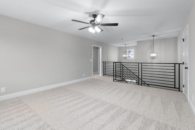 carpeted empty room with ceiling fan with notable chandelier and baseboards