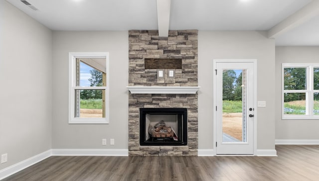 unfurnished living room featuring visible vents, beamed ceiling, wood finished floors, a fireplace, and baseboards