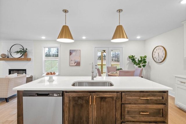 kitchen featuring light wood finished floors, dishwasher, light countertops, plenty of natural light, and a sink