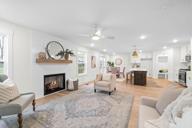 living room featuring light wood-style flooring, a ceiling fan, recessed lighting, a fireplace, and baseboards