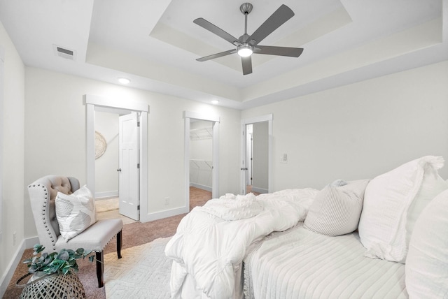 carpeted bedroom featuring visible vents, a walk in closet, a ceiling fan, baseboards, and a raised ceiling