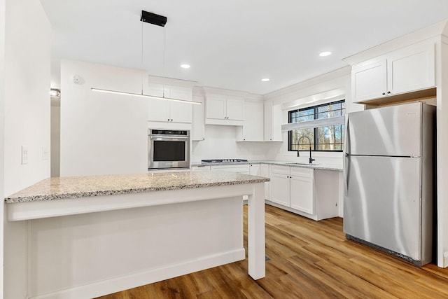 kitchen with light stone counters, stainless steel appliances, light wood-style floors, and a sink