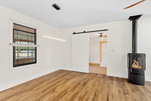 unfurnished room with baseboards, visible vents, light wood finished floors, ceiling fan, and a barn door