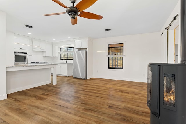 kitchen featuring a ceiling fan, wood finished floors, a barn door, appliances with stainless steel finishes, and white cabinets