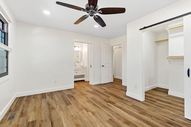 unfurnished bedroom with a barn door, light wood-style floors, visible vents, and baseboards