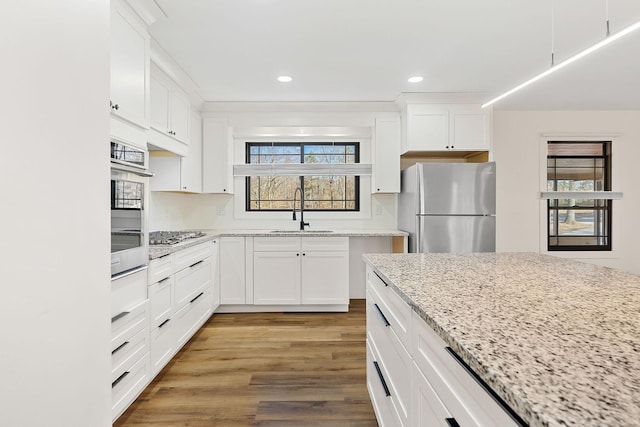 kitchen featuring light wood-style flooring, a sink, appliances with stainless steel finishes, white cabinets, and light stone countertops