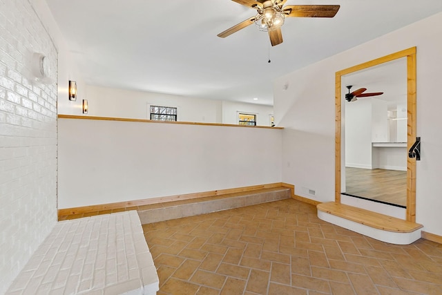 basement featuring visible vents, brick wall, a ceiling fan, and baseboards