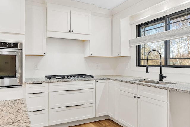 kitchen with light wood-type flooring, light stone counters, white cabinets, stainless steel appliances, and a sink