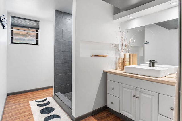 full bathroom featuring baseboards, a tile shower, recessed lighting, wood finished floors, and vanity