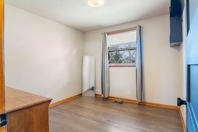 spare room with a textured ceiling, baseboards, and wood finished floors