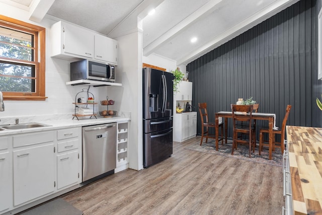 kitchen featuring a sink, light wood-style floors, appliances with stainless steel finishes, and vaulted ceiling with beams