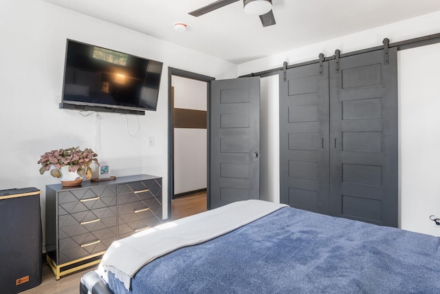 bedroom featuring a barn door, wood finished floors, and ceiling fan