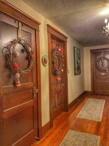 corridor featuring an inviting chandelier, wood finished floors, baseboards, and a textured ceiling