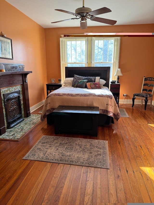 bedroom featuring baseboards, a ceiling fan, hardwood / wood-style floors, and a fireplace