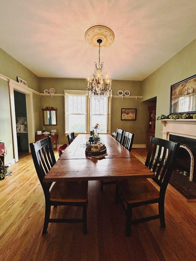 dining space featuring a fireplace with raised hearth, baseboards, an inviting chandelier, and wood finished floors