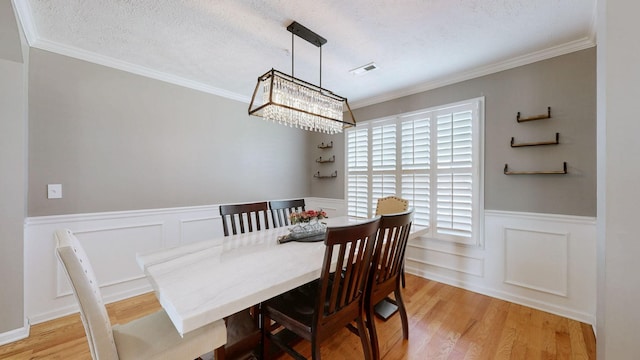 dining room with visible vents, light wood-style flooring, ornamental molding, a textured ceiling, and wainscoting