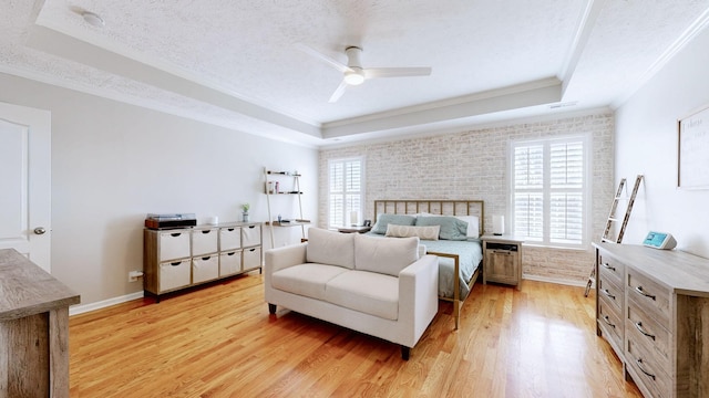 bedroom featuring brick wall, a textured ceiling, a raised ceiling, and light wood-style floors